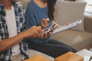 Two Asian blogger showing clothes in front of the camera to recording vlog video live streaming at her shop. Online Shopping Cart notion. on sofa at home photo