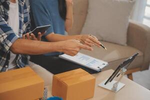 Two Asian blogger showing clothes in front of the camera to recording vlog video live streaming at her shop. Online Shopping Cart notion. on sofa at home photo