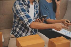 Two Asian blogger showing clothes in front of the camera to recording vlog video live streaming at her shop. Online Shopping Cart notion. on sofa at home photo