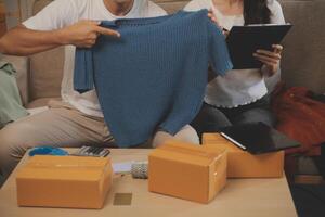 Two Asian blogger showing clothes in front of the camera to recording vlog video live streaming at her shop. Online Shopping Cart notion. on sofa at home photo