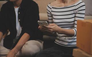Two Asian blogger showing clothes in front of the camera to recording vlog video live streaming at her shop. Online Shopping Cart notion. on sofa at home photo