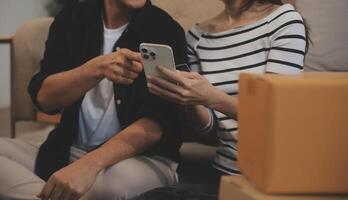 Two Asian blogger showing clothes in front of the camera to recording vlog video live streaming at her shop. Online Shopping Cart notion. on sofa at home photo