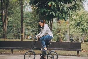 contento asiático joven mujer caminar y paseo bicicleta en parque, calle ciudad su sonriente utilizando bicicleta de transporte, eco amigable, personas estilo de vida concepto. foto