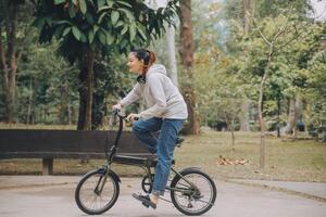 contento asiático joven mujer caminar y paseo bicicleta en parque, calle ciudad su sonriente utilizando bicicleta de transporte, eco amigable, personas estilo de vida concepto. foto