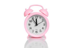 pink alarm clock set twelve o'clock isolated over white background photo