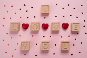 Inscription I love you on wooden cubes. Hearts on a pink background and confetti hearts. photo