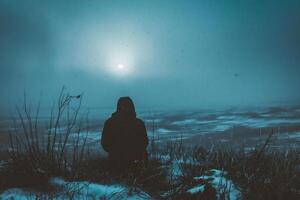 AI generated Silhouette of a man sitting on the top of a mountain and looking at the moon photo