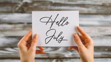 AI generated Hands holding a card with the word Hello July on wooden background photo