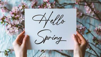 AI generated Hello Spring. Hello spring card with woman hands holding a white sheet of paper with spring blossom background photo