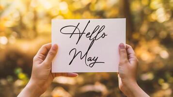 AI generated cropped view of woman holding card with hello may lettering near blooming tree photo