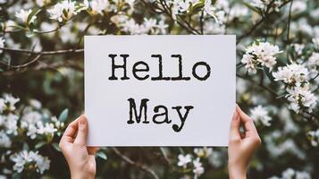 AI generated cropped view of woman holding card with hello may lettering near blooming tree photo