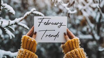 AI generated Female hands in yellow sweater holding white paper sheet with February Trends text on snowy background. photo