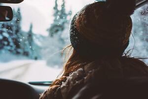 ai generado un joven mujer es conducción un coche en un Nevado invierno la carretera. foto