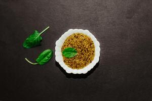 grain mustard with a green leaf in a white bowl on a black background. photo