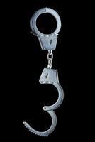 real zinc plated steel police handcuffs half-opened hanging vertically, isolated on black background photo