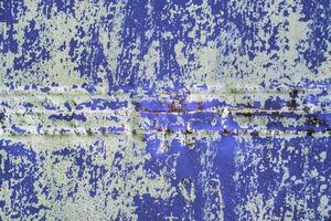 blue steel sheet wall with peeled off white paint under direct sunlight, full-frame background and texture photo