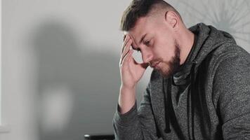 Pensive Man in Studio with Headache, Young adult male holding his head, showing signs of stress or headache in a modern studio setting. video