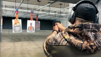 Man Practicing Shooting at Indoor Range, Person in camo attire aiming a handgun at targets in a shooting range, focusing on precision and safety. video