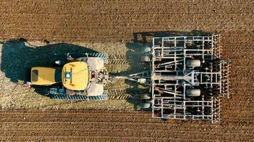 aérien Haut vue une tracteur charrues une champ avec une herse système. préparation de agricole terre pour printemps semis. video