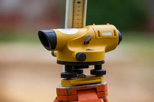 Yellow theodolite on a tripod and a ruler with a blurred background. Geodetic measurements. photo