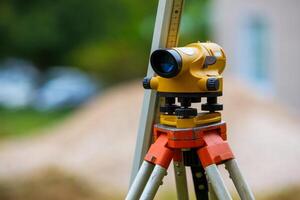 Yellow theodolite on a tripod and a ruler with a blurred background. Geodetic measurements. photo