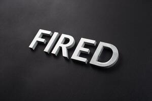 the word fired laid with silver metal letters on flat black surface photo