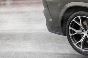 rain water splashing flows from wheels of grey car that moving fast on asphalt road photo