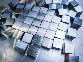 pile of small machined shiny steel cubes on metal surface photo