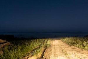 dry dirt road in the middle of nowhere lit with car headlights at early foggy morning photo