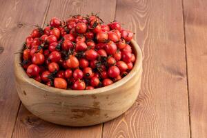 red dog-rose rosehip fruits in a wooden bowl on wooden table photo