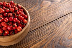 red dog-rose rosehip fruits in a wooden bowl on wooden table photo