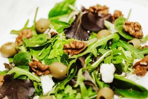 Salad leaves with arugula, cheese, green olives and nuts in a plate, healthy diet salad. photo