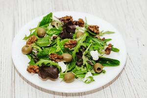 Salad leaves with arugula, cheese, green olives and nuts in a plate, healthy diet salad. photo