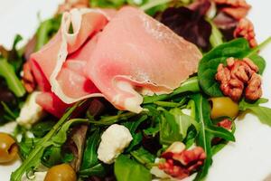 Salad with herbs, arugula, prosciutto, cheese, green olives and nuts. photo