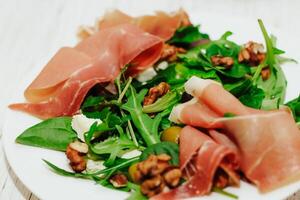 Salad with herbs, arugula, prosciutto, cheese, green olives and nuts. photo