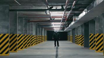 Security guard in the underground parking lot. Large underground parking without cars. A man inspects the parking lot video