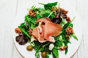 Salad with herbs, arugula, prosciutto, cheese, green olives and nuts. photo