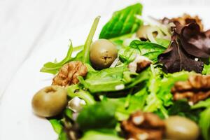 Salad leaves with arugula, cheese, green olives and nuts in a plate, healthy diet salad. photo