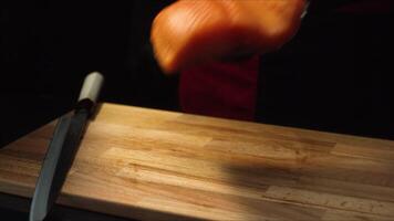 Close-up chef with piece of red salmon. Professional chef in black apron and gloves puts piece of salmon on wooden board before slicing it for dishes video