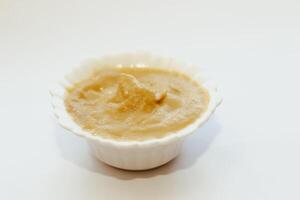 Mustard sauce in a white bowl on a white table. photo