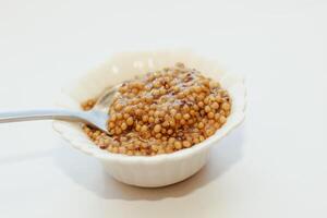 grano mostaza en un blanco cuenco en un blanco mesa. foto