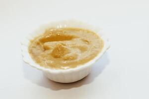 Mustard sauce in a white bowl on a white table. photo