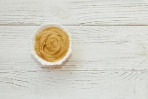 Mustard sauce in a white bowl on a white table. photo