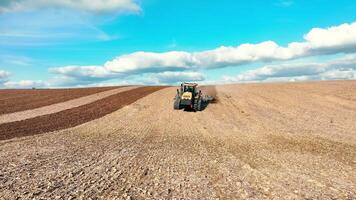 aéreo ver un tractor arados un campo con un grada sistema. preparación de agrícola tierra para primavera siembra. video