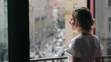 un contento caucásico mujer es en pie por el ventana, sonriente y mirando a un hermosa ramo. esperando por el ventana. video