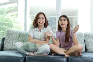 asian woman and friend sit at home on sofa bed watch tv movie. photo