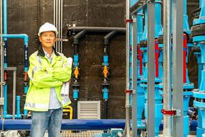 asian man worker in protective uniform and with hardhat using tablet for checking temperature in pipes Factory interior. photo