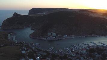 Antenne Aussicht von schön Hafen Stadt gelegen auf das Bucht Ufer in der Nähe von das Meer und umgeben durch hoch Hügel gegen das Sonnenuntergang Himmel. Schuss. malerisch Aussicht von das klein Stadt, Dorf video