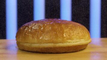 Close up of hamburger bun cut in two. Stock footage. Wheat burger bun lying on wooden surface with flying flour on black background with blue stripes. video