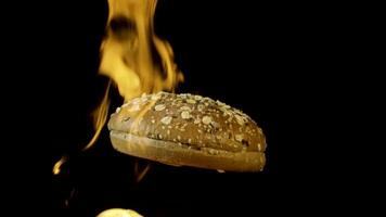 An appetizing burger bun with sesame seeds isolated on black background with red flame. Stock footage. Food and cooking concepr, rotating baked bun in flame. video